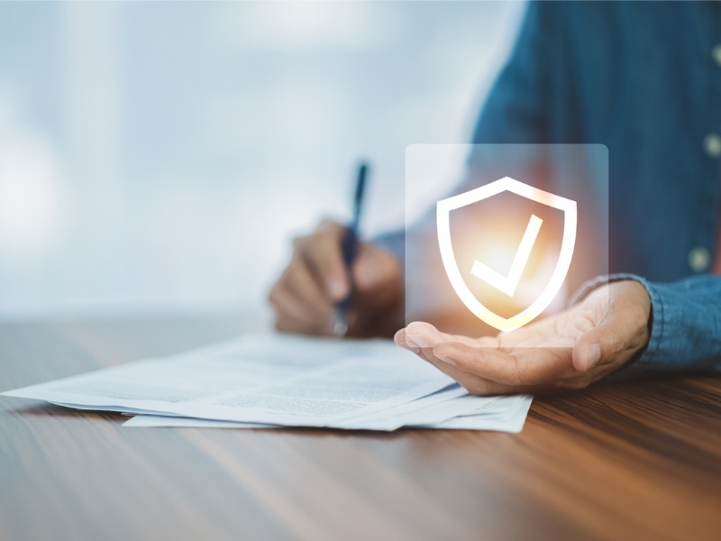 Man signing document, with one of his hands holding the symbol of a checkmark within a shield
