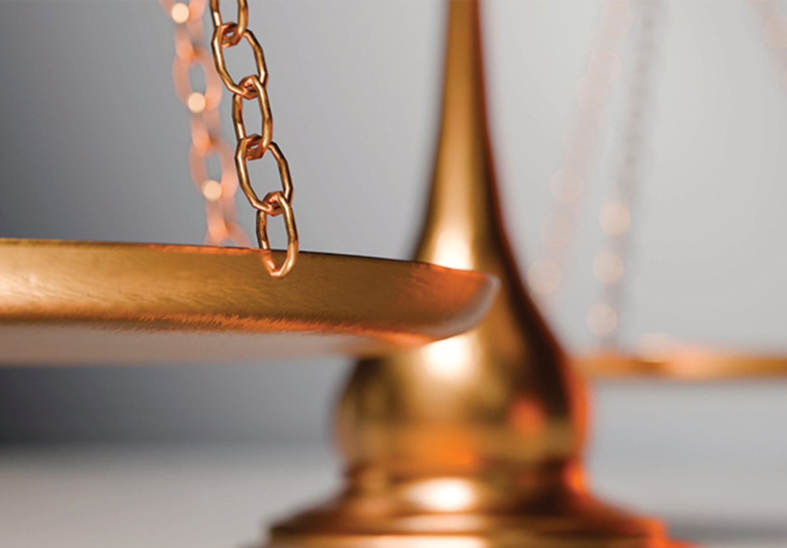 Close of gold-colored balance scale, with one suspended weighing pan in sharp focus.